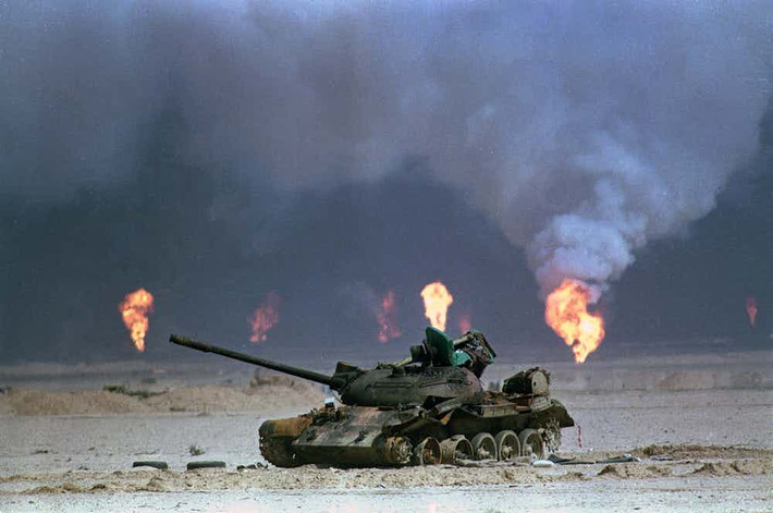 Một chiếc xe tăng Iraq bị phá hủy trong cuộc chiến tranh ác liệt ở Iraq. Phía sau là những giếng dầu bốc cháy ngùn ngụt.
