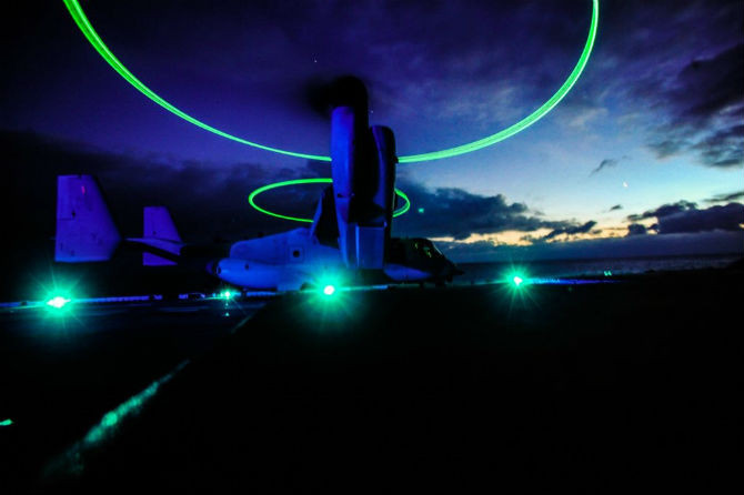 Đèn hiệu đầu mút cánh của máy bay MV-22 Osprey bật sáng khi chuẩn bị cất cánh từ tàu đổ bộ USS Boxer (LHD-4), lớp Wasp. Osprey là máy bay có thiết kế lai độc đáo giữa trực thăng và máy bay cánh cố định cho phép cất, hạ cánh thẳng đứng.