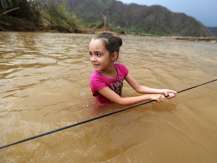 Siêu bão Maria mạnh cấp 4 đã tàn phá Puerto Rico vào ngày 20/9 và gây ra cuộc khủng hoảng nhân đạo tại hòn đảo này. Do ảnh hưởng của bão, cho đến nay phần lớn Puerto Rico bị mất điện. Ngoài ra, thực phẩm, nước uống và nhiều mặt hàng cần thiết khác đều khan hiếm. Ảnh: Bé Ruby Rodriguez (8 tuổi) lội qua sông ở Morovis. Ảnh: BI.
