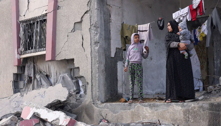 Các cuộc giao tranh giữa Israel và lực lượng Hamas đã kéo dài nhiều tháng, làm ảnh hưởng đến cuộc sống của người dân ở Gaza. Ảnh: Một phụ nữ Palestine bế con đứng trước ngôi nhà bị hư hại trong đợt oanh kích của Israel tại Rafah ngày 27/2.