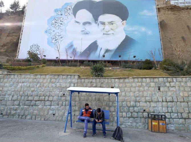 Hai thanh niên người Iran ngồi trong một công viên ở Tehran ngày 17/1/2016. Phía sau họ là bức hình lớn về cố lãnh tụ Iran Ayatollah Ruhollah Khomeini (trái) và lãnh đạo tối cao của Iran Ayatollah Ali Khamemei.