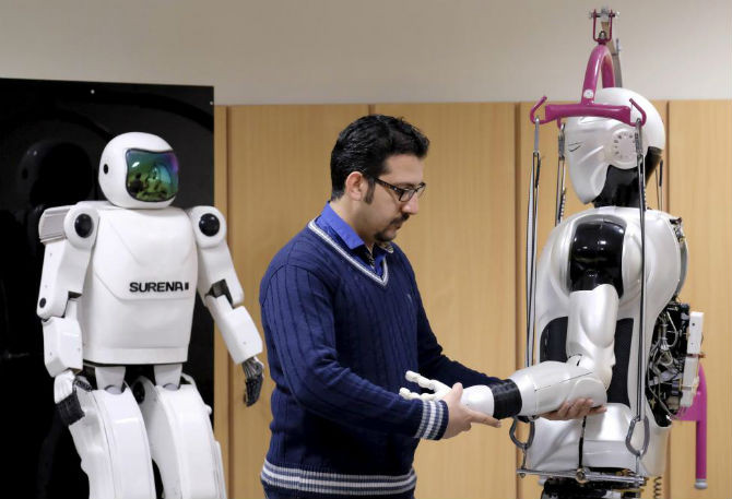 Kỹ sư Iran đang kiểm tra chú robot Surena 3 (phải) cạnh robot Surena 2 trong phòng thí nghiệm tại trường Đại học Tehran ngày 6/12/2015. Trường Đại học Tehran phát triển một loại robot giống hình dáng con người nặng 98 kg. Nó có thể di chuyển trên địa hình không bằng phẳng.