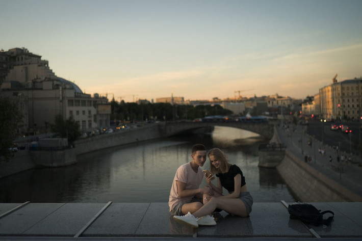 Cặp đôi ngồi xem điện thoại trên cây cầu ở thủ đô Moscow lúc hoàng hôn ngày 26/6.