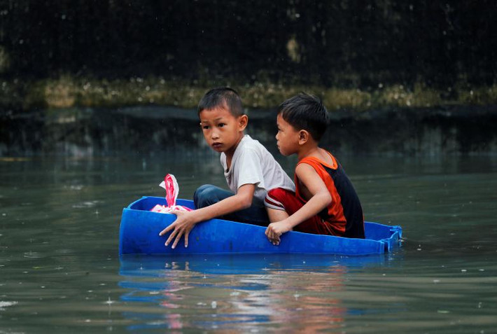 Hai em nhỏ ngồi trên chiếc bè tạm bợ để di chuyển trong khu vực chìm trong biển nước. Mời độc giả xem thêm video: Bão Fung Wong gây mưa lớn và ngập lụt tại Philippines năm 2014 (Nguồn: VTC14)