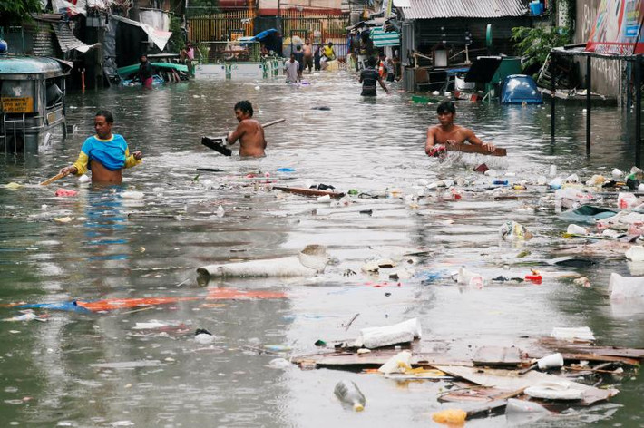 Người dân thu gom rác thải trên con đường ngập nước ở thành phố Quezon, Vùng đô thị Manila.