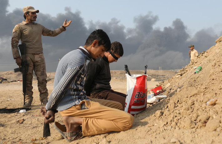 Một binh sĩ Iraq đứng sau hai chiến binh bị cáo buộc là thành viên tổ chức khủng bố IS đang quỳ gối tại một chốt kiểm soát ở Qayyara hôm 27/10.