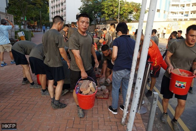 Họ mặc quần ngắn đen, áo phông và mang theo chổi, xô chậu rời doanh trại đồn trú ở Cửu Long vào khoảng 16h chiều 16/11 để dọn chướng ngại vật trên đường Renfrew, gần khuôn viên Trường Đại học Baptist Hong Kong. Ảnh: HKFP.