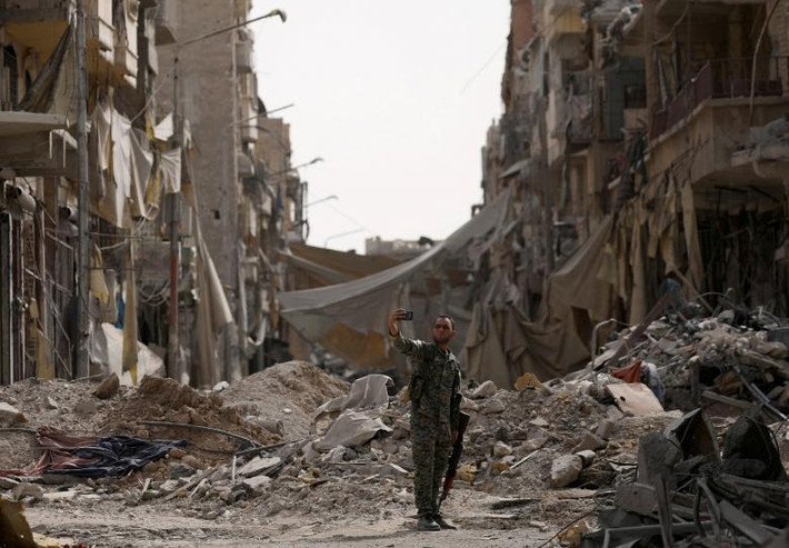 Chiến binh SDF chụp ảnh “tự sướng” trước đống đổ nát ở thành phố Raqqa. Ảnh: Reuters.
