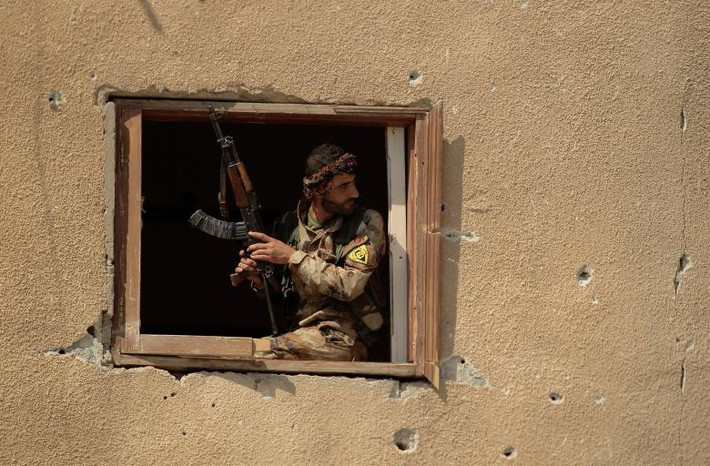 Tay súng SDF quan sát khi ngồi phía trước căn cứ của IS ở Raqqa. Ảnh: Reuters.