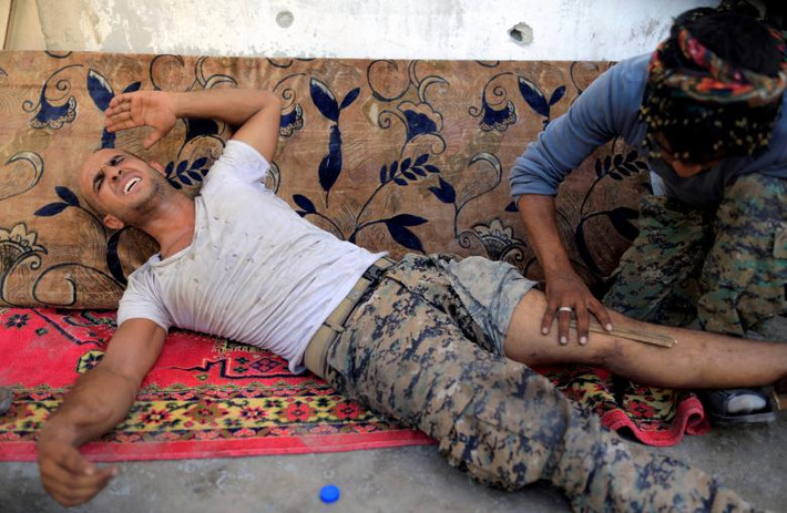 Một chiến binh SDF bị gãy chân trong cuộc giao tranh với IS ở Raqqa đang được đồng đội băng bó. Ảnh: Reuters.