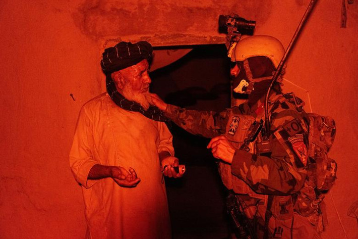 Một thành viên của lực lượng đặc nhiệm Afghanistan nói chuyện với người dân khi những người khác lục soát ngôi nhà trong cuộc chiến chống Taliban tại tỉnh Kandahar ngày 12/7.