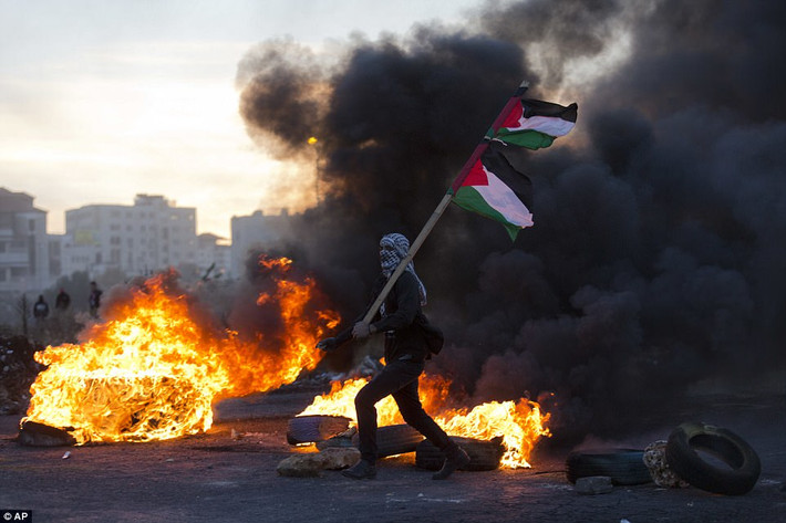 Một người biểu tình mang theo cờ Palestine đi qua đống lửa trong cuộc biểu tình phản đối quyết định của Tổng thống Trump. Ảnh: AP.