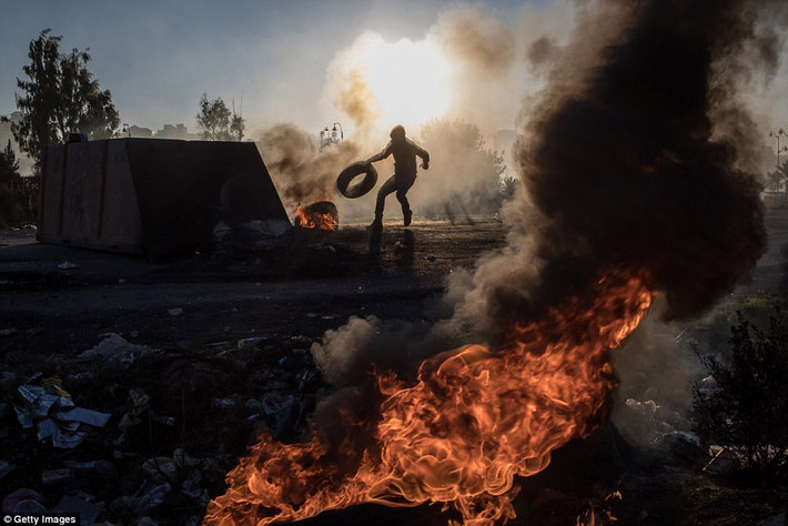 Ở Đông Jerusalem, cảnh sát Israel đã bắt giữ tất cả những người Palestine chặn đường. Nhiều thùng rác bị đốt cháy và tiếng lựu đạn nổ thường xuyên vang lên. Ảnh: Một người biểu tình Palestine đốt lốp xe trong cuộc đụng độ với lực lượng biên phòng Israel gần một chốt kiểm soát ở Ramallah. Ảnh: Getty Images.