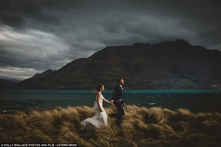 Cặp vợ chồng trẻ nắm tay nhau đi qua cánh đồng ở Queenstown, New Zealand.