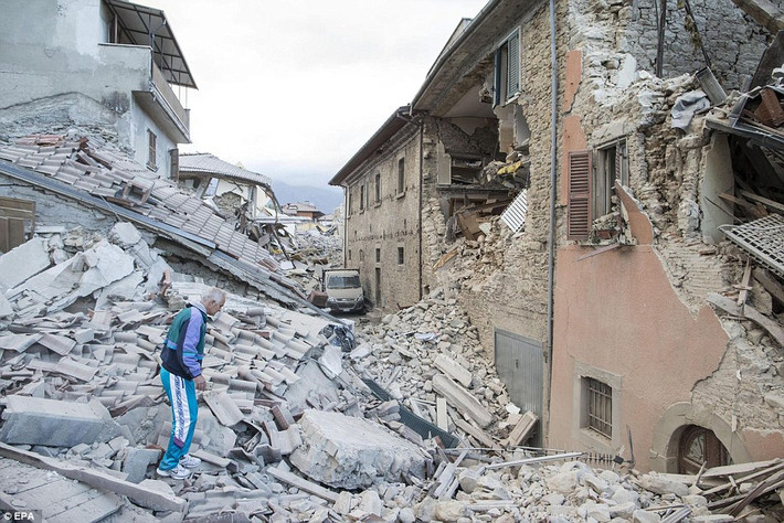 Một người đàn ông đứng giữa đống đổ nát ở Amatrice.