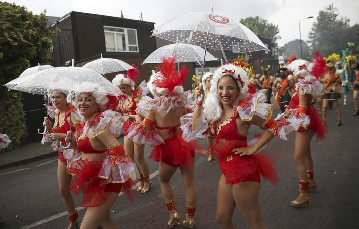 Những cô gái vừa cầm ô vừa diễu hành dưới trời mưa tại lễ hội Notting Hill Carnival.
