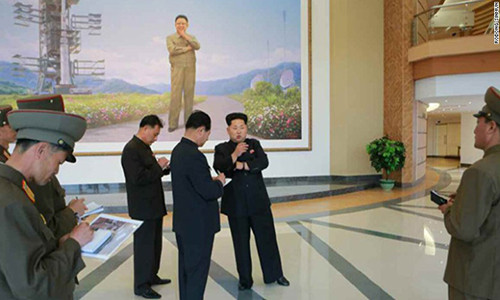 Nhà lãnh đạo Kim Jong-un đứng trao đổi trong trung tâm. Phía sau ông có một bức tranh lớn cố Chủ tịch Kim Jong-il.
