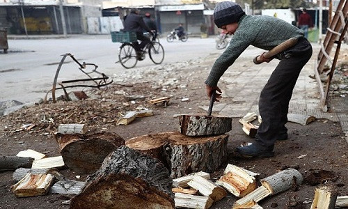 Một người dân Syria đứng bổ củi bên lề đường.