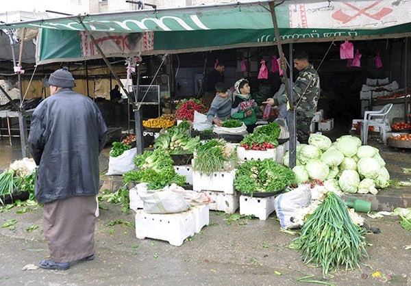 Người đàn ông Syria đi qua một quầy hàng bán rau xanh.