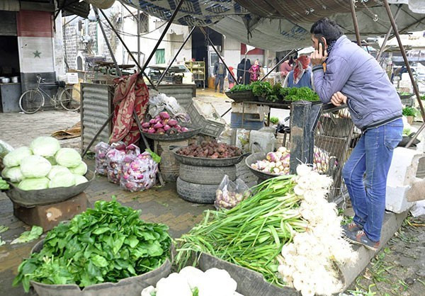 Một người đàn ông đứng nghe điện thoại trước quầy hàng bán rau củ trong khu chợ địa phương ở Hama.