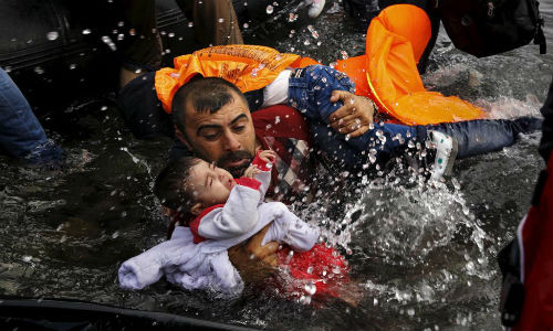 Một người tị nạn Syria bế hai con trên tay cố gắng xuống thuyền khi tới đảo Lesbos, Hy Lạp, ngày 24/9/2015.