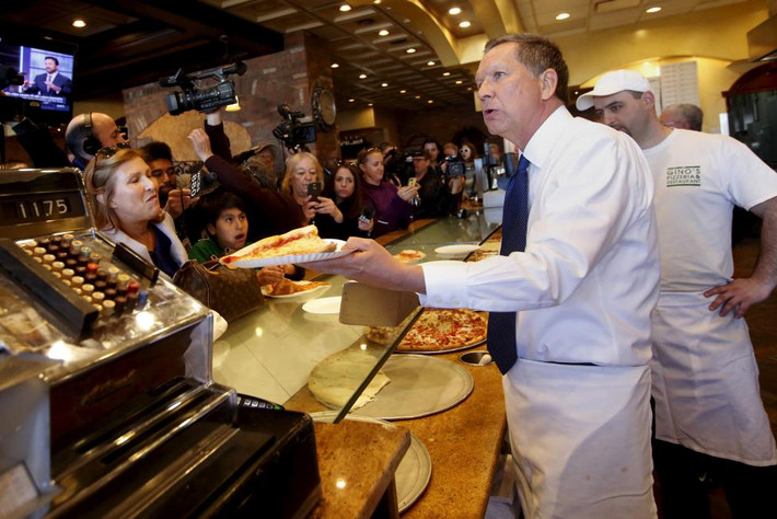 Thống đốc bang Ohio bê đĩa pizza cho thực khách tại nhà hàng Gino ở Queens, New York, ngày 30/3.