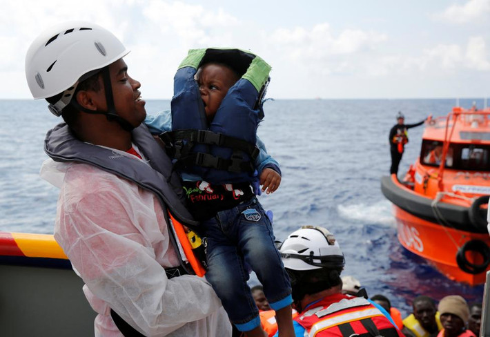 Một nhân viên cứu hộ bế em bé di dân lên tàu Topaz Responder ngoài khơi bờ biển Libya.