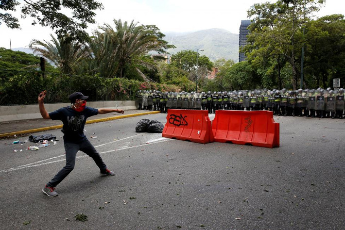Một người biểu tình ném đá về phía cảnh sát chống bạo động ở thủ đô Caracas.