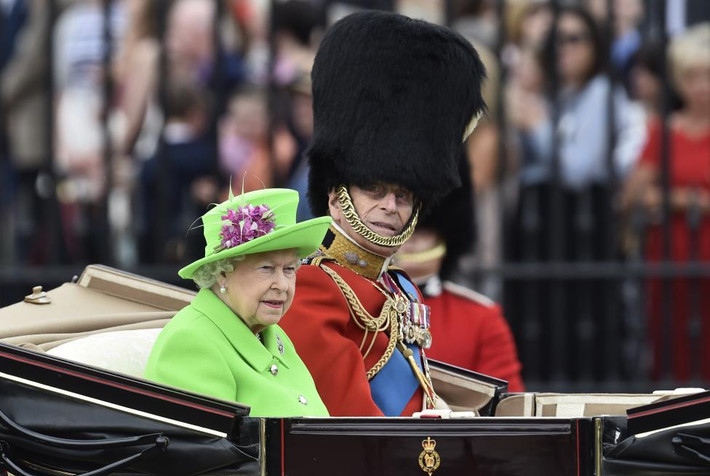 Nữ hoàng Elizabeth II ngồi trên xe ngựa kéo và diễu qua đám đông dân chúng trong bộ váy và mũ xanh nổi bật, bên cạnh là Hoàng tế Philip.