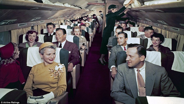 Hành khách chờ máy bay cất cánh khi ngồi trong cabin máy bay Douglas DC-7. Trong ảnh, các hành khách nữ đeo gang tay, mặc váy và đội mũ trong khi hành khách nam mặc comple và thắt cà vạt.