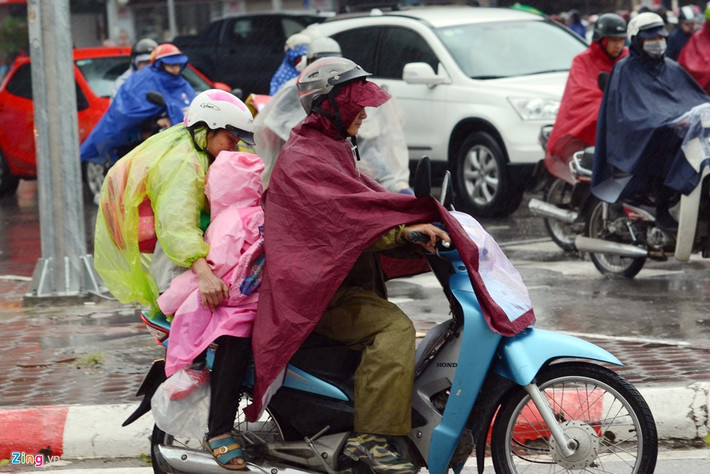 Một phụ huynh cho con nhỏ ngồi ngược lại tránh gió, còn người lái xe máy loay hoay giữa dòng người trong sự vướng víu của chiếc áo mưa. Ảnh: Tiến Tuấn.