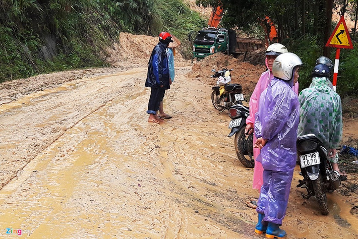 Một đoạn đường bị vùi lấp bởi lượng lớn đất đá khiến mạch giao thông bị cắt đứt. Người dân đứng chờ lực lượng chức năng dùng xe chuyên dụng san ủi, tạo lối đi.