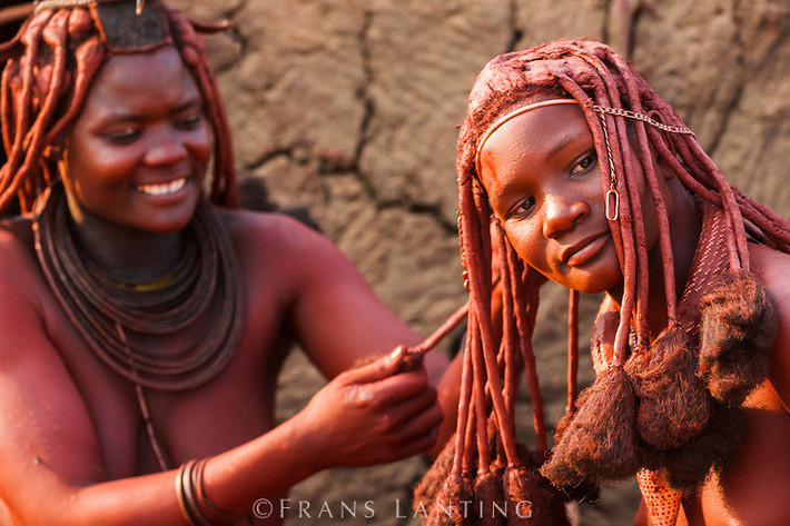 Bộ tộc Himba, Namibia: Phụ nữ của tộc Himba nổi tiếng với tóc và làn da ánh đỏ. Họ bôi otjize - một hỗn hợp gồm bơ, mỡ và đất đỏ - lên tóc và da hàng ngày. Nhiều người cho rằng otjize giúp tránh nắng và chống côn trùng, nhưng tộc Himba cho biết họ dùng chúng chỉ hoàn toàn vì lý do thẩm mỹ. Ảnh: Frans Lanting.