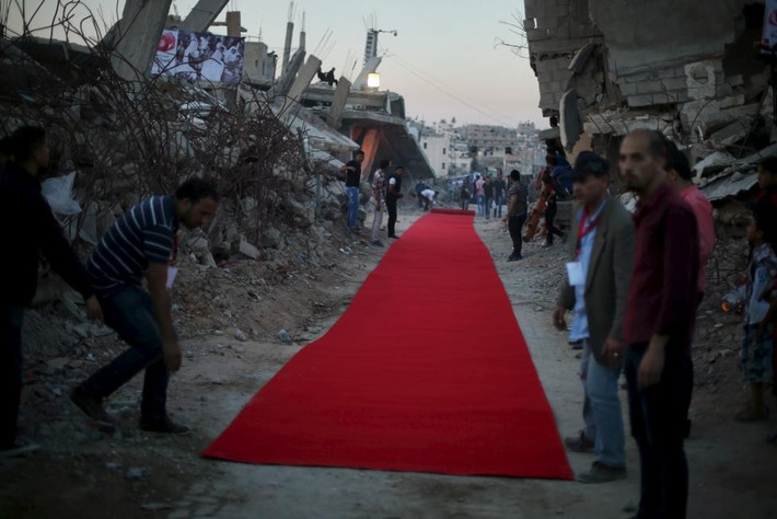 Người dân Palestine trải thảm đỏ giữa những ngôi nhà bị phá hủy dở trong chiến dịch không kích kéo dài 50 ngày của Israel trong mùa hè năm 2014. Họ chuẩn bị chiếu một bộ phim về chiến tranh ở phía đông thành phố Gaza hôm 12/5. Vào những tháng cuối năm nay, căng thẳng tiếp tục leo thang vì các vụ tấn công bằng dao từ phía người phản đối Palestine với binh lính Israel, dẫn tới những vụ tấn công đáp trả của binh sĩ nhà nước Do Thái. Ảnh: Reuters