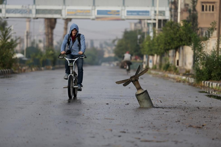 Người dân đạp xe qua đoạn đường có quả bom chưa nổ ở thị trấn Douma, miền Đông Ghouta, Damascus, Syria hôm 5/11. Gần 5 năm qua, cuộc nội chiến Syria không những không có dấu hiệu kết thúc mà còn ngày càng trở nên phức tạp hơn với sự tham gia của nhiều phe phái. Cuối tháng 9, Nga phát động chiến dịch không kích các phần tử nổi dậy ở Syria, bao gồm cả tổ chức khủng bố IS. Moscow không giấu mục tiêu bảo vệ chính quyền Tổng thống Bashar al-Assad trong khi các nước phương Tây muốn lật đổ nhân vật này để dựng một chính phủ thân phương Tây ở Syria. Ảnh: Reuters