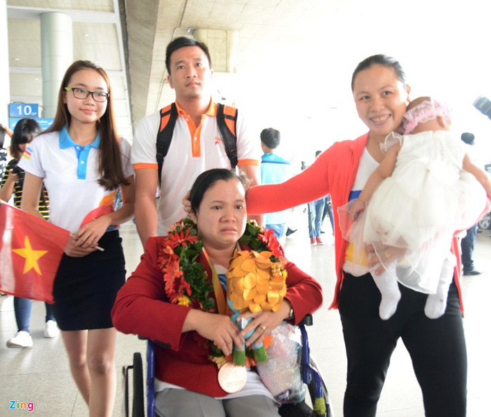 VĐV Đặng Thị Linh Phượng bật khóc khi về đến Việt Nam. Tại giải đấu vừa qua, cô đã giành HCĐ hạng cân dưới 50 kg nữ ở môn cử tạ. Vợ của Lê Văn Công, chị Chu Thị Tám vừa bế con vừa an ủi đồng nghiệp của chồng.
