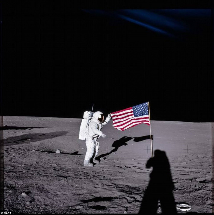 Phi hành gia Alan Bean của tàu Apollo 12 cắm cờ trên Mặt Trăng trong khi người chỉ huy con tàu vũ trụ này (đứng bên phải) chỉ hiện lên qua một cái bóng dài.