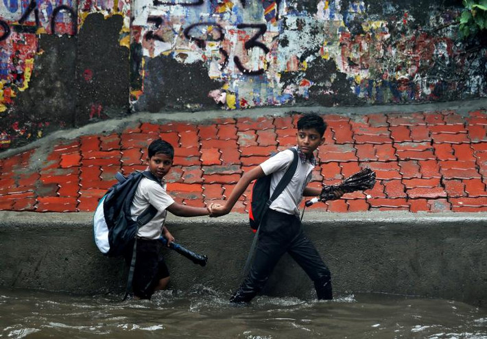 Hai em nhỏ đi qua con đường ngập nước đến trường sau mưa lớn ở thành phố Mumbai. Ảnh: Reuters.