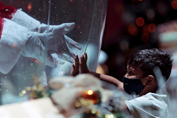 "Ông già Noel" Abilio da Cruz Pinto, 77 tuổi, đứng trong quả cầu nhựa ở trung tâm thương mại Brasilia, Brazil, khi giao lưu với một em nhỏ đeo khẩu trang phòng COVID-19 hôm 15/12.