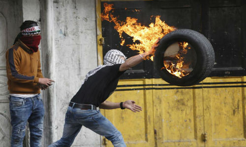 Một người biểu tình Palestine ném lốp xe đang bốc cháy về phía binh sĩ Israel.