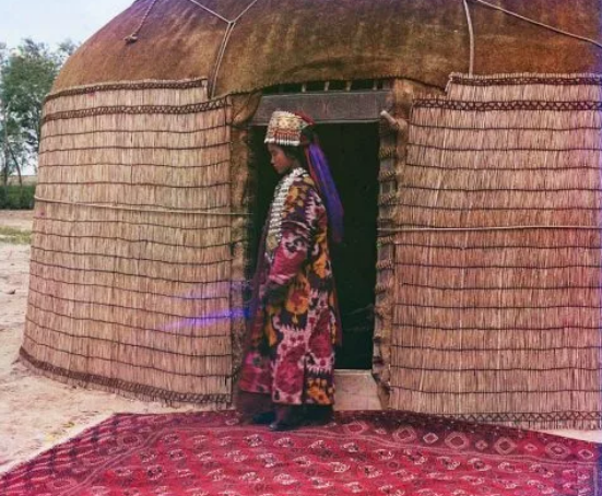 Người phụ nữ mặc trang phục dân tộc đứng trước túp lều yurt.