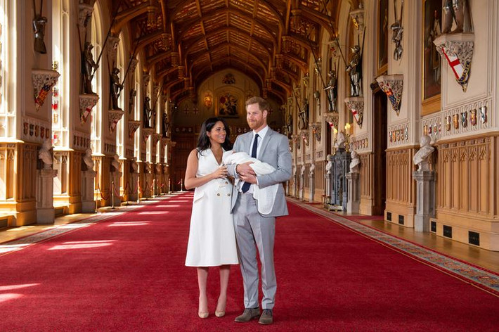 Hoàng tử Harry bế con trong khi Công nương Meghan Markle đứng cạnh. Ảnh: Daily Mail.