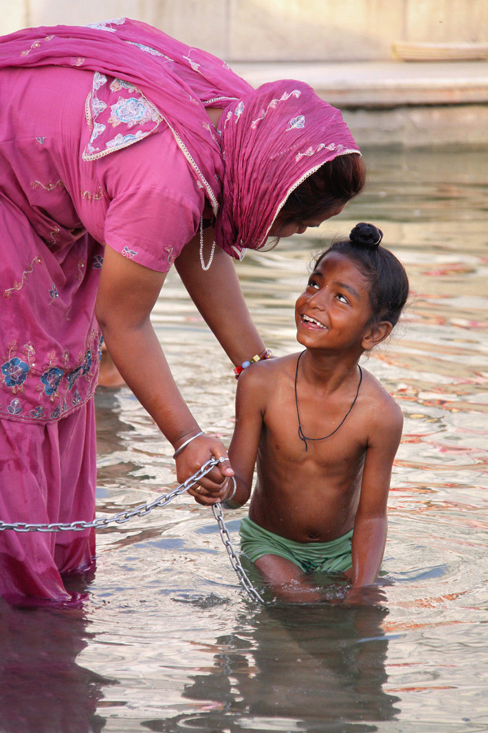 Người mẹ tắm cho con trai trong dòng nước thánh của ngôi Đền Vàng ở Amritsar, Ấn Độ.