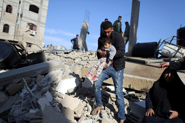 Một người đàn ông Palestine bế em nhỏ qua đống đổ nát tại một ngôi nhà bị phá hủy bởi các cuộc không kích từ phía Israel, phía nam Dải Gaza, ngày 5/5.