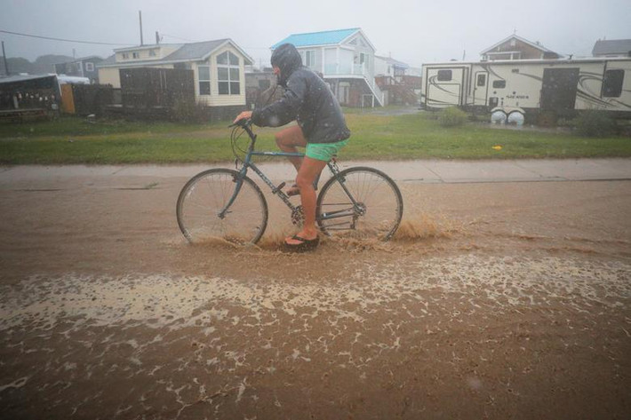 Một người đạp xe qua con đường ngập lụt ở South Kingstown, Rhode Island, ngày 22/8. Ảnh: Reuters.