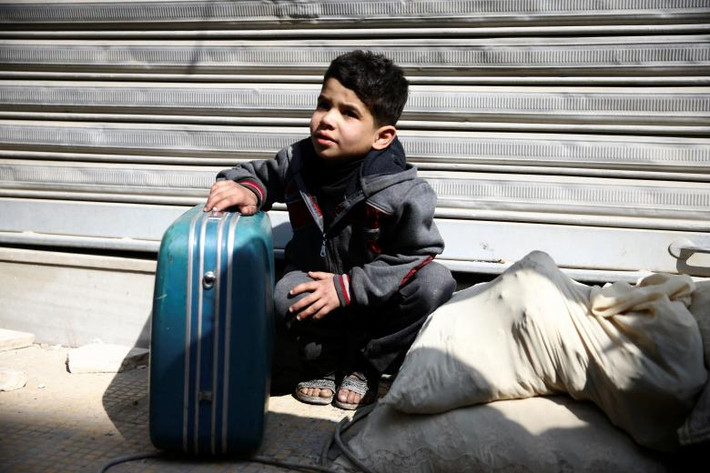 Một bé trai giữ hành lý trong lúc chờ người thân tại thị trấn Douma, Đông Ghouta. Ảnh: Reuters.