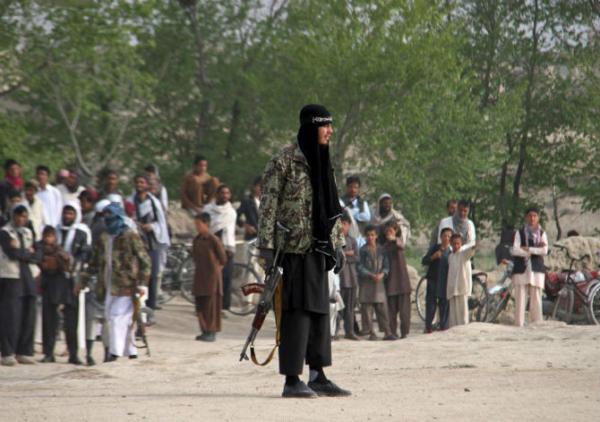 Một chiến binh của phong trào Taliban và những người khác đứng tại khu vực nơi vụ hành quyết ba người đàn ông tại tỉnh Ghazni diễn ra.