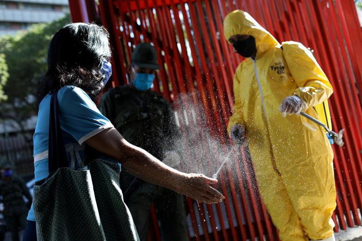 Nhân viên phun thuốc khử trùng vào tay một khách hàng tại lối vào khu chợ công cộng ở Caracas, Venezuela, hôm 18/3.