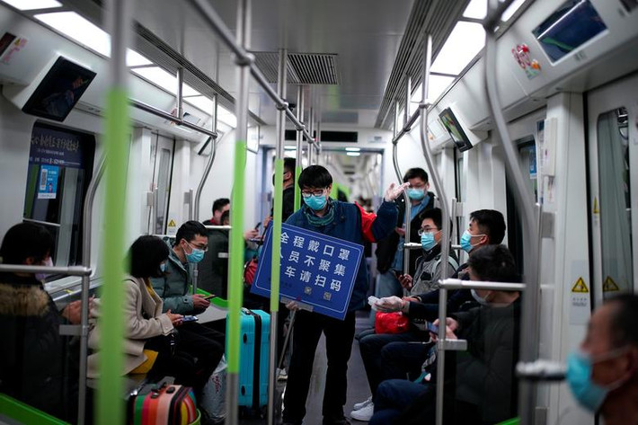 Một nhân viên trên tàu điện ngầm đeo khẩu trang và giữ tấm bảng có dòng chữ với nội dung: "Luôn đeo khẩu trang, tránh tụ tập, quét mã khi xuống tàu" sau khi dịch vụ được nối lại ở Vũ Hán hôm 28/3.