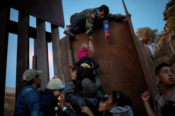 Các di dân đến từ Honduras đang tìm cách đưa một em nhỏ qua bức tường biên giới ở Tijuana, Mexico, ngày 2/12.